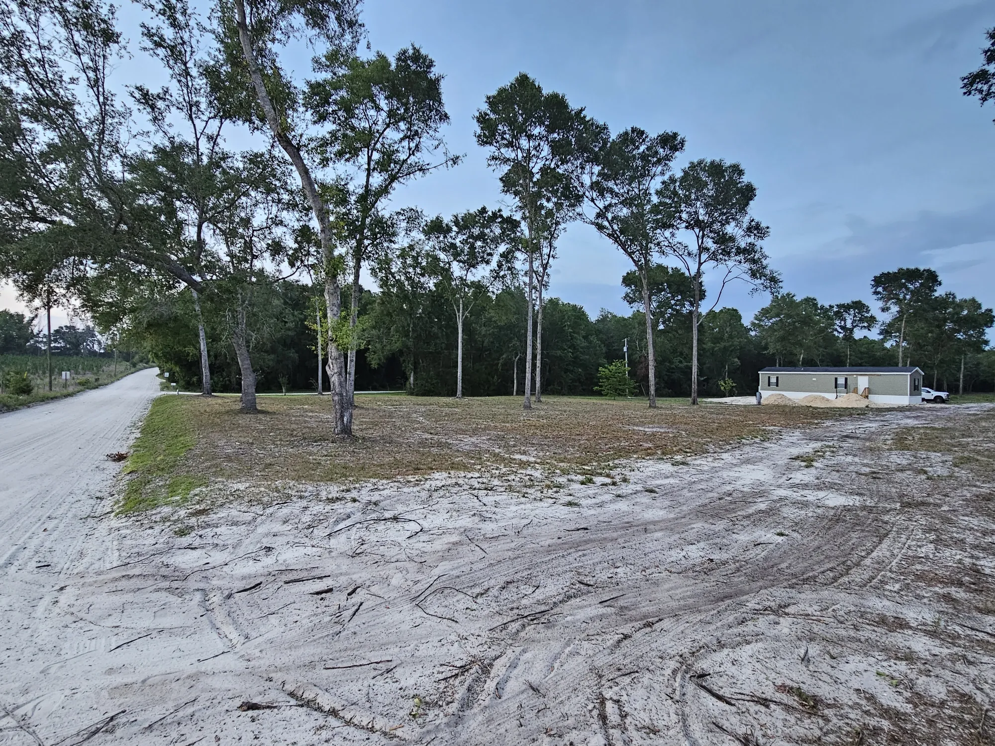 Rural property access driveway with cleared land and mobile home visible in the background